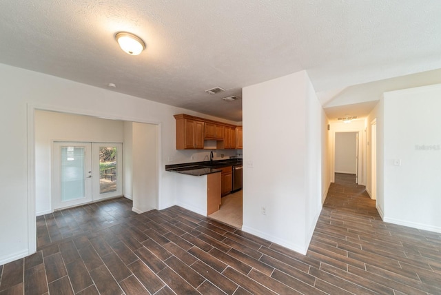 kitchen featuring dark countertops, dark wood-style floors, a sink, stainless steel dishwasher, and baseboards