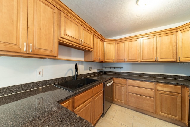 kitchen featuring a sink, stainless steel dishwasher, light tile patterned flooring, brown cabinets, and dark stone counters