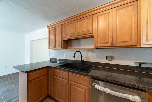 kitchen featuring a sink, stainless steel dishwasher, a peninsula, dark stone countertops, and a textured ceiling
