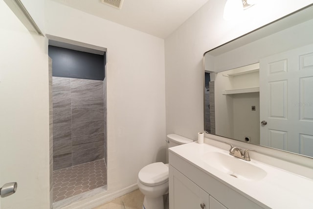 bathroom with toilet, a tile shower, tile patterned flooring, and vanity