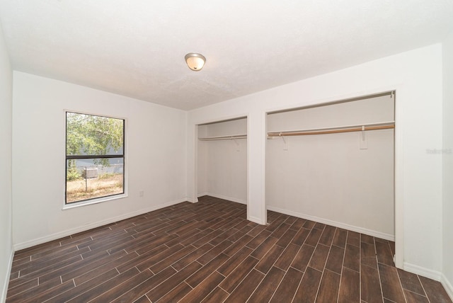 unfurnished bedroom with multiple closets, dark wood-type flooring, and baseboards