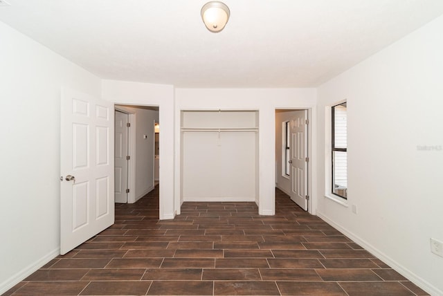 unfurnished bedroom featuring dark wood-style floors, a closet, and baseboards