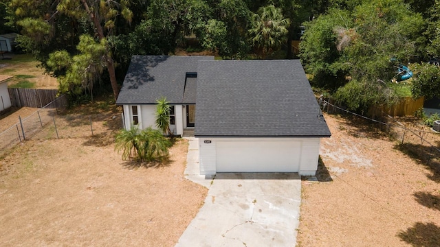 view of front of property with concrete driveway, a garage, a shingled roof, and fence
