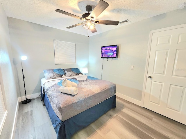 bedroom featuring light wood-style flooring, baseboards, a textured ceiling, and ceiling fan