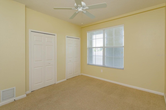 unfurnished bedroom with two closets, carpet flooring, baseboards, and ceiling fan