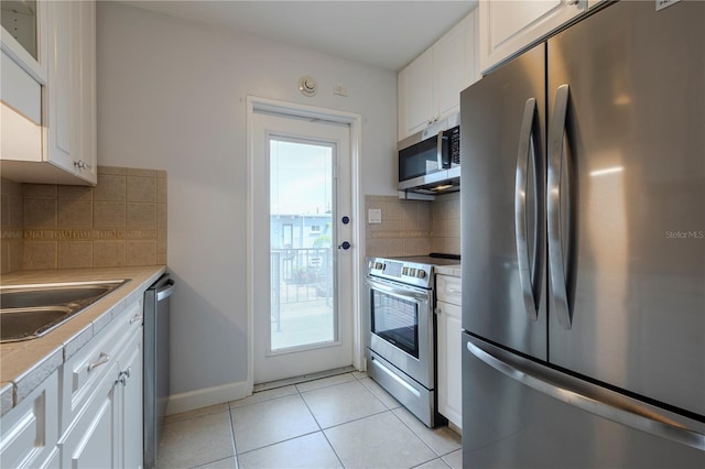kitchen with appliances with stainless steel finishes, white cabinetry, light tile patterned flooring, and backsplash