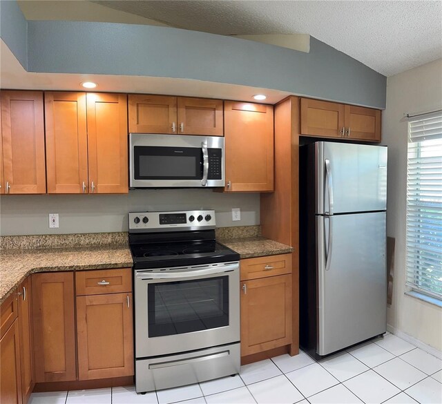 14844 Laguna Beach Cir, Orlando, FL 32824 - kitchen with appliances with stainless steel finishes, brown cabinetry, light tile patterned flooring, lofted ceiling, and a textured ceiling