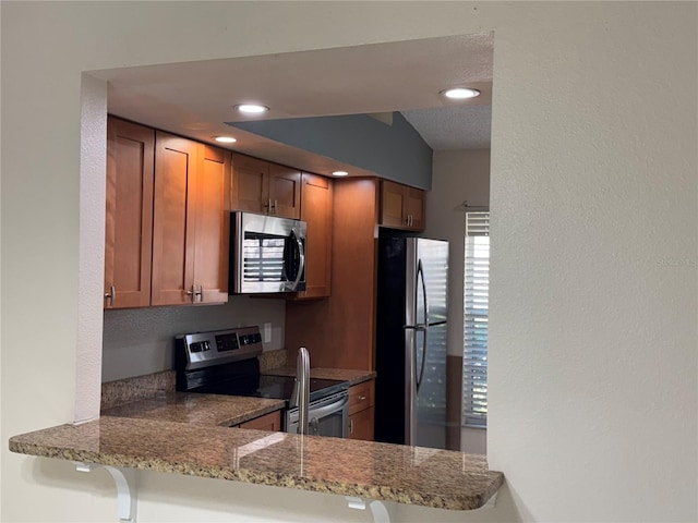 14844 Laguna Beach Cir, Orlando, FL 32824 - kitchen featuring appliances with stainless steel finishes, brown cabinets, a peninsula, a textured wall, and stone counters
