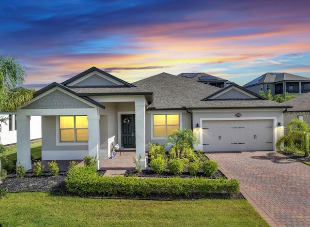 ranch-style home with a shingled roof, a garage, stucco siding, decorative driveway, and a front yard
