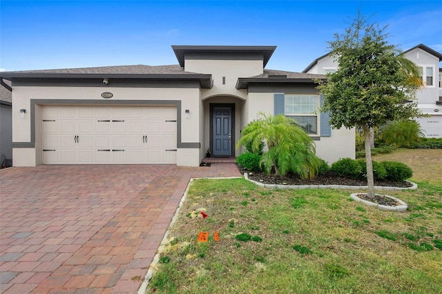 view of front of house featuring decorative driveway, stucco siding, a garage, and a front yard