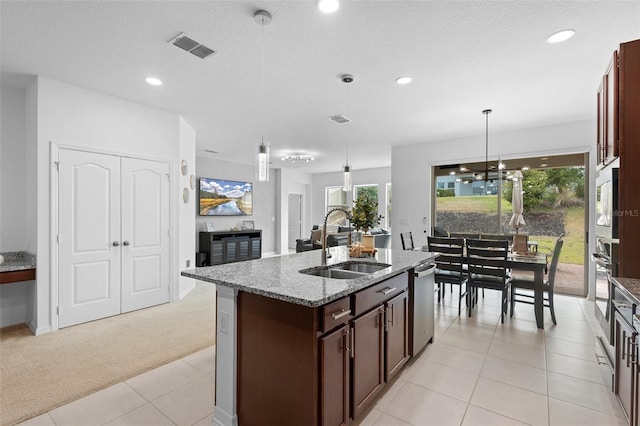 kitchen with a sink, stainless steel appliances, light carpet, light stone counters, and a kitchen island with sink