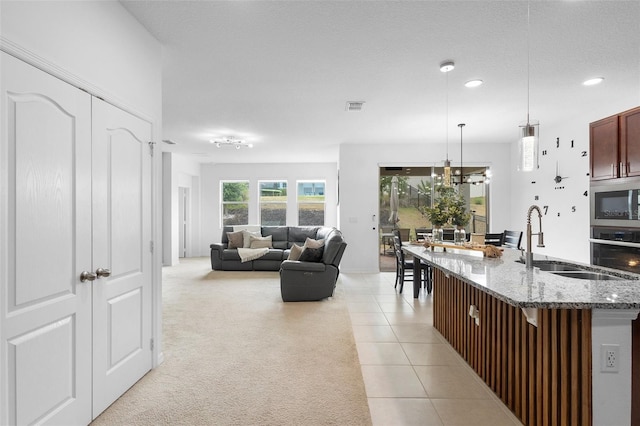 kitchen with a sink, stainless steel appliances, pendant lighting, light stone counters, and recessed lighting