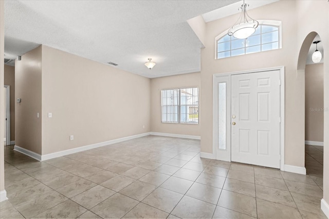 tiled foyer featuring arched walkways, baseboards, and a textured ceiling