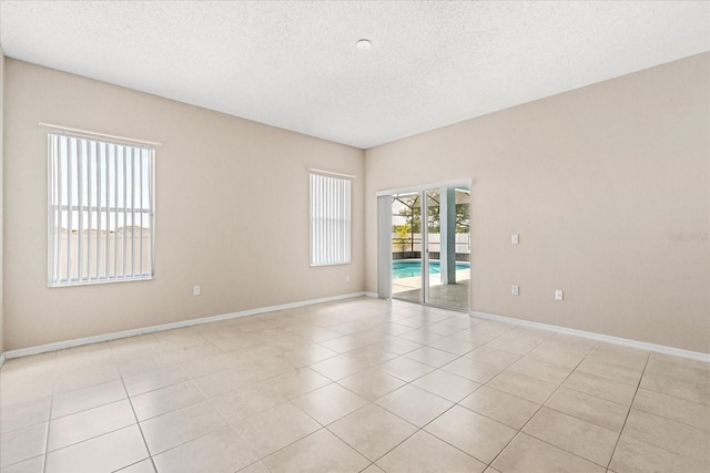 empty room with a textured ceiling, baseboards, and light tile patterned flooring