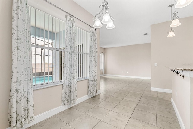 tiled empty room featuring baseboards and a chandelier