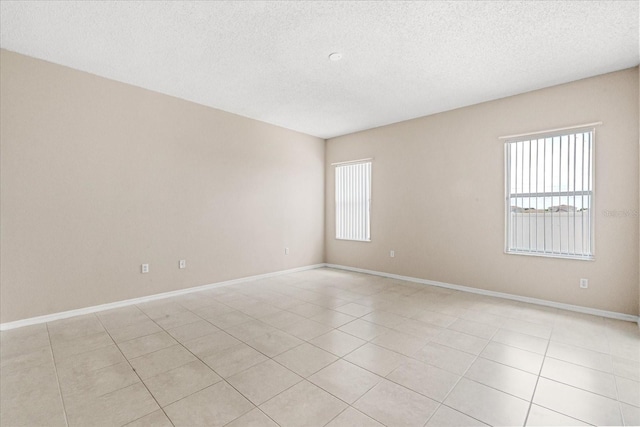 empty room featuring a textured ceiling, healthy amount of natural light, baseboards, and light tile patterned flooring