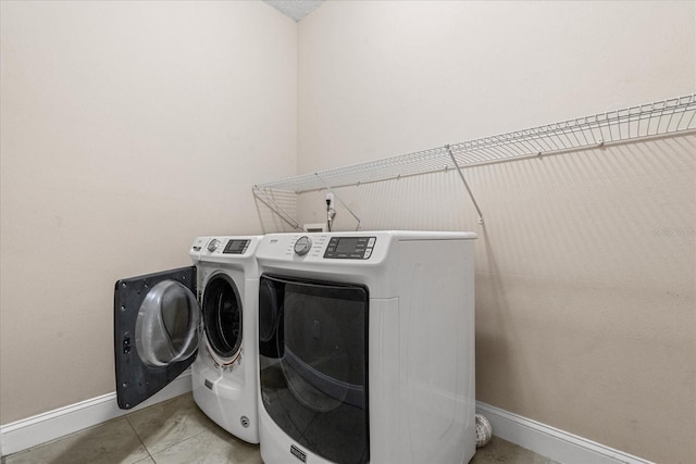 clothes washing area with baseboards, washer and dryer, and tile patterned floors