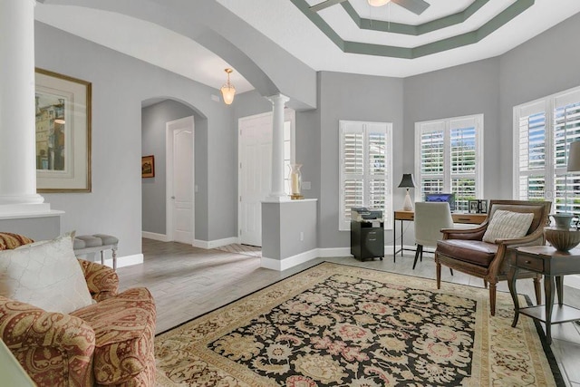 living area with arched walkways, a ceiling fan, baseboards, wood finished floors, and decorative columns