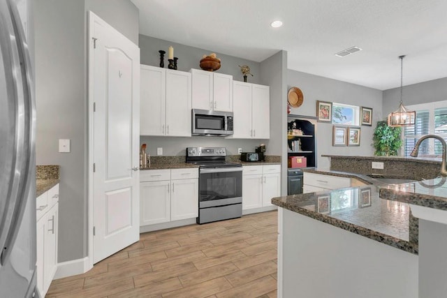 kitchen featuring appliances with stainless steel finishes, a sink, light wood-type flooring, white cabinets, and decorative light fixtures