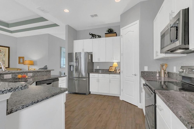 kitchen featuring appliances with stainless steel finishes, light wood finished floors, white cabinetry, recessed lighting, and dark stone counters