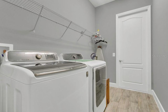 washroom featuring washing machine and dryer, baseboards, and light wood-type flooring