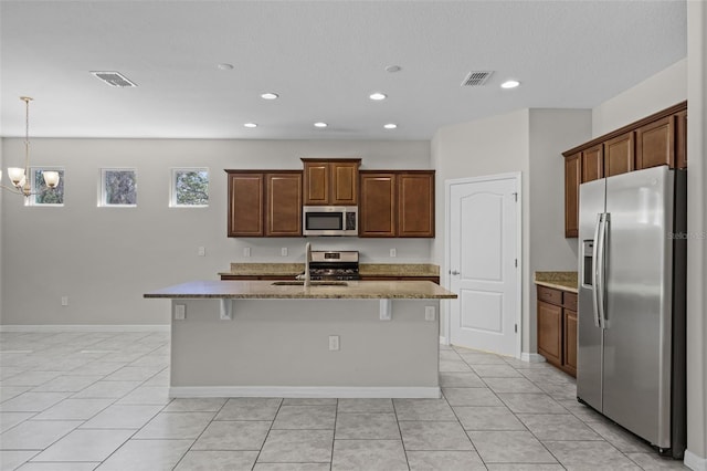 kitchen with stainless steel appliances, a sink, recessed lighting, an island with sink, and light stone counters