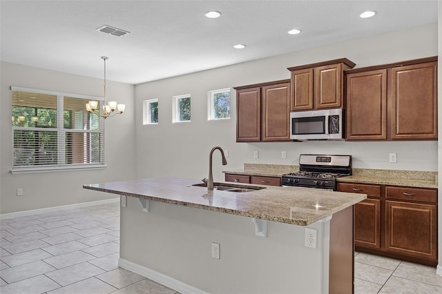 kitchen featuring stainless steel appliances, a sink, a kitchen island with sink, a kitchen bar, and light stone countertops