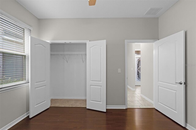 unfurnished bedroom with multiple windows, wood finished floors, baseboards, and a closet