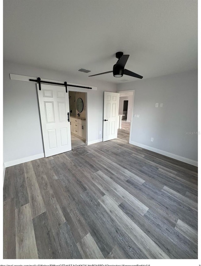 unfurnished bedroom with a barn door, wood finished floors, baseboards, and ceiling fan