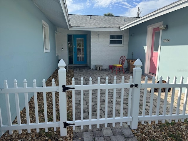 view of exterior entry featuring fence, a gate, brick siding, and a shingled roof