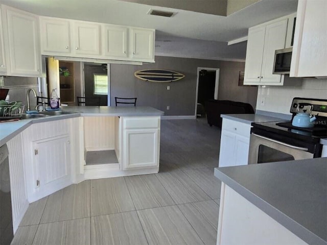 kitchen with appliances with stainless steel finishes, a sink, white cabinetry, and a peninsula