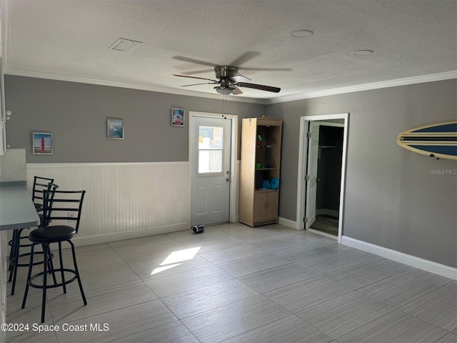 empty room featuring a ceiling fan, a textured ceiling, crown molding, and wainscoting