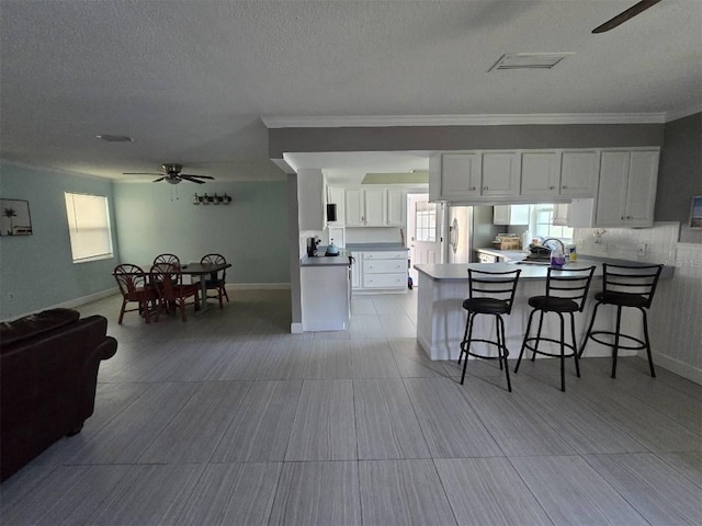 kitchen featuring ceiling fan, open floor plan, a peninsula, a kitchen breakfast bar, and white cabinets
