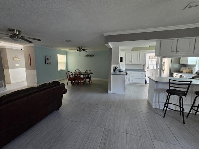 living area with ceiling fan, ornamental molding, a textured ceiling, and baseboards