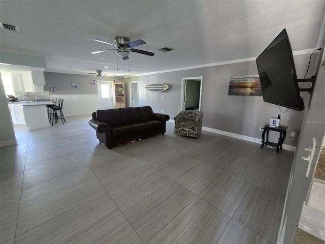living room with a ceiling fan, baseboards, ornamental molding, and a textured ceiling