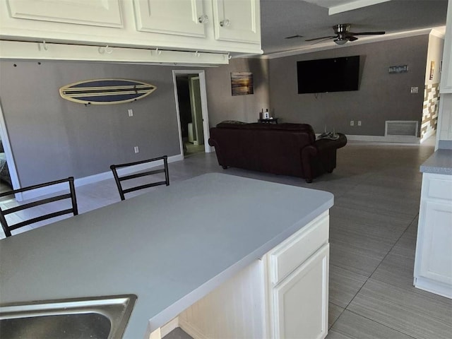 kitchen with ceiling fan, open floor plan, white cabinets, and baseboards