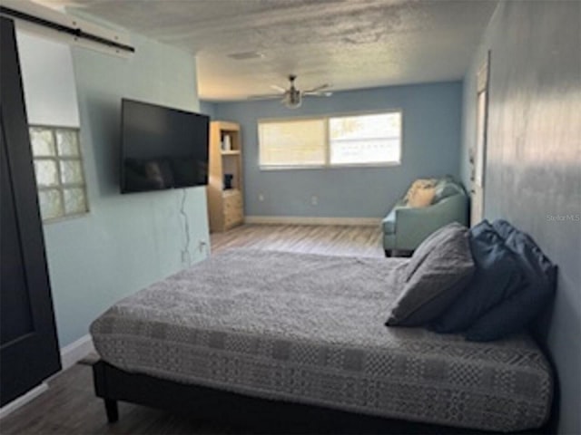bedroom featuring a barn door, wood finished floors, baseboards, and a ceiling fan
