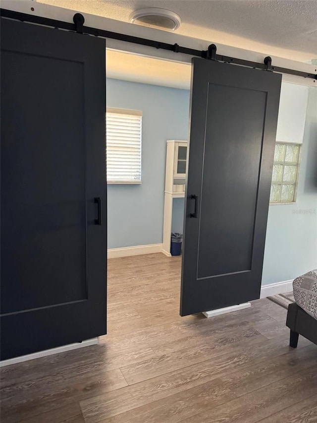 interior space with a barn door, wood finished floors, baseboards, and a textured ceiling