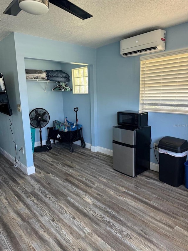 bedroom with an AC wall unit, freestanding refrigerator, wood finished floors, a textured ceiling, and baseboards