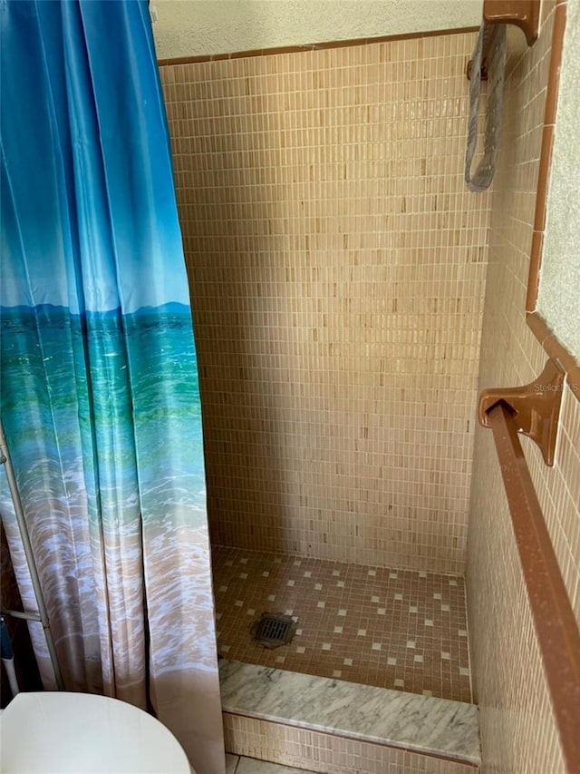 bathroom featuring tiled shower, toilet, and tile walls