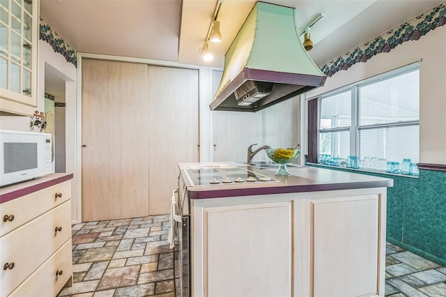 kitchen with island exhaust hood, white microwave, electric range, track lighting, and light stone finish floors
