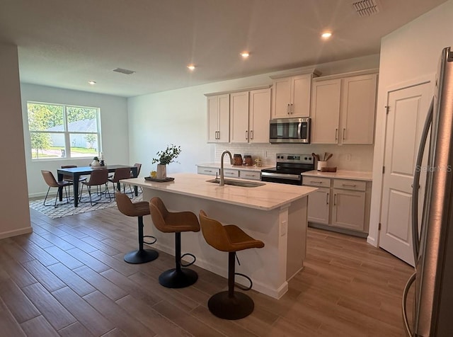 2681 Ginseng Ivy St, Apopka, FL 32703 - kitchen featuring stainless steel appliances, backsplash, wood finished floors, a kitchen breakfast bar, and a kitchen island with sink