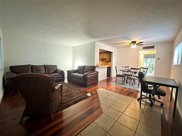 living area with a ceiling fan, light wood-style flooring, and a textured ceiling