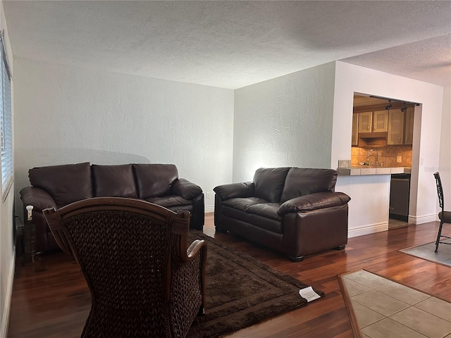 living room with a textured wall, dark wood-style floors, a textured ceiling, and baseboards
