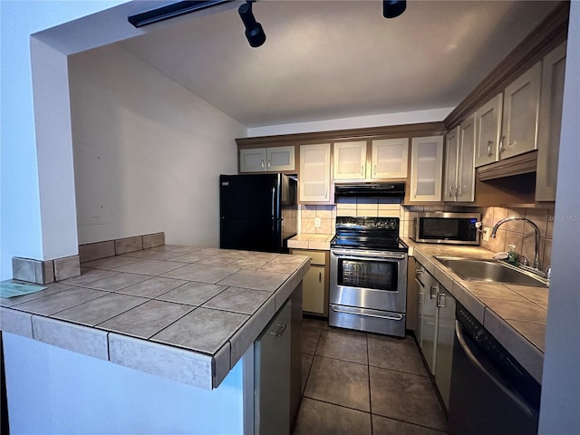 kitchen with appliances with stainless steel finishes, tile countertops, range hood, a sink, and tasteful backsplash