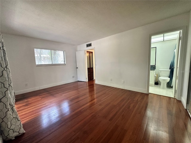 unfurnished bedroom with hardwood / wood-style flooring, a textured ceiling, baseboards, and ensuite bathroom