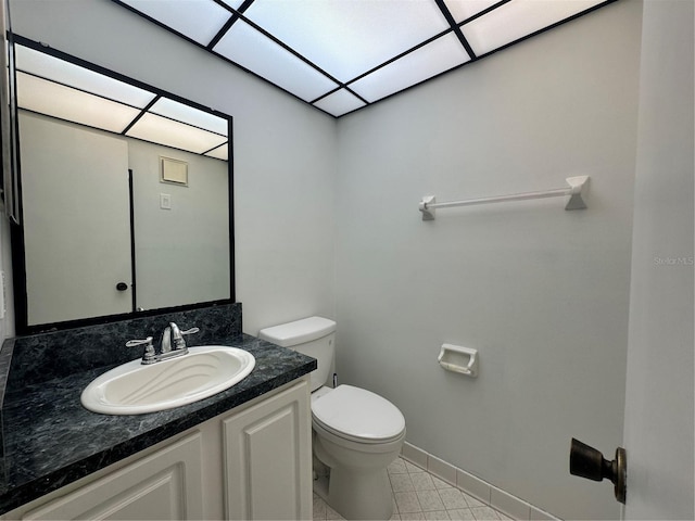 half bathroom featuring toilet, vanity, baseboards, and tile patterned floors