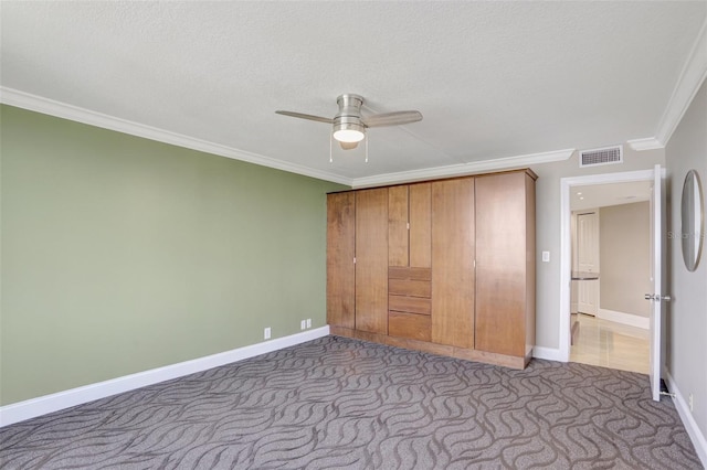 unfurnished bedroom featuring ornamental molding, carpet, baseboards, a ceiling fan, and a textured ceiling