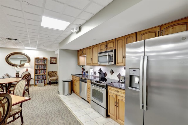 kitchen featuring appliances with stainless steel finishes, dark countertops, decorative backsplash, light carpet, and brown cabinets