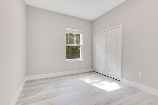 unfurnished bedroom featuring light wood-style flooring, baseboards, and a closet
